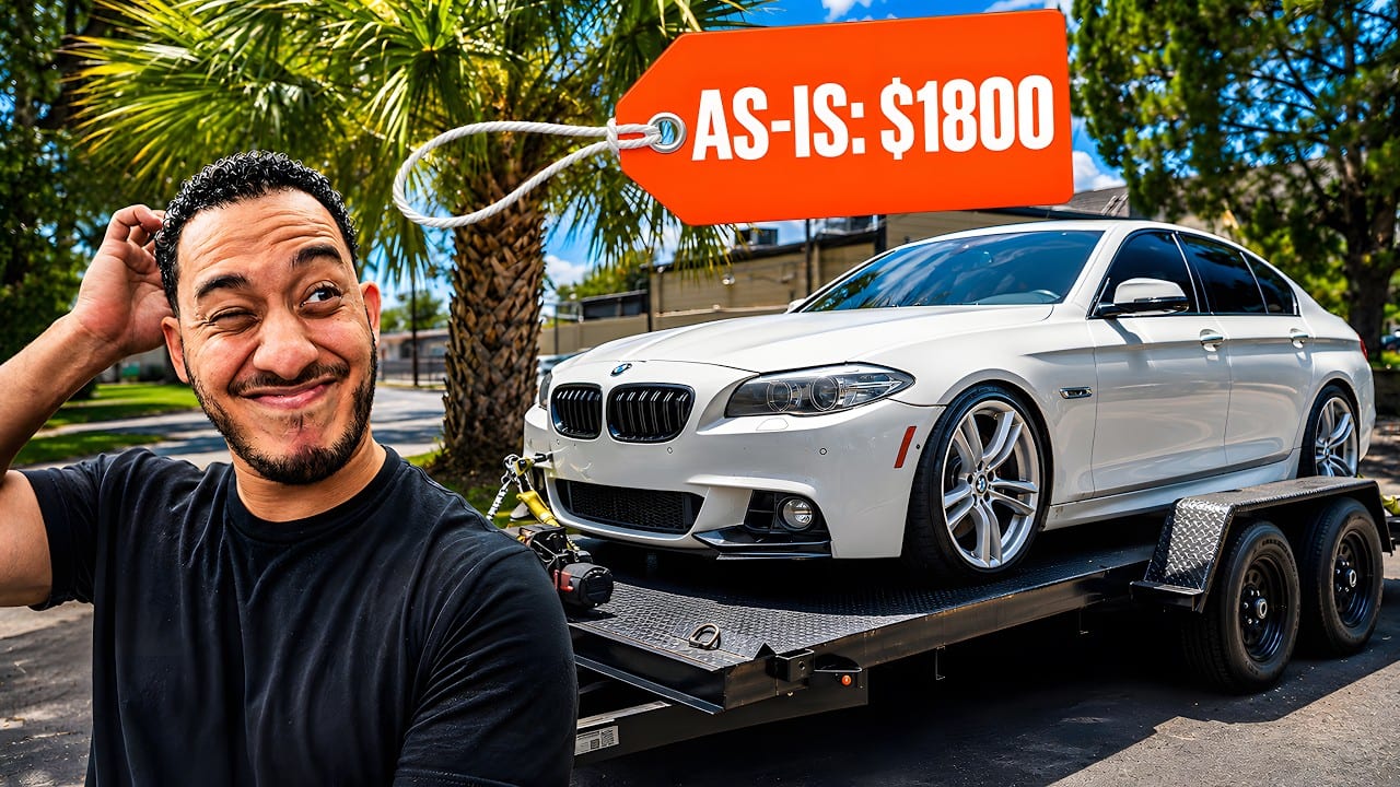The original thumbnail: a presenter scratching his head in the foreground, a spotless white BMW on a flatbed trailer behind him, and an orange swing tag reading AS-IS: $1800